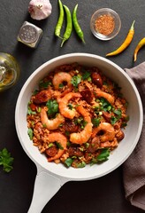 Creole jambalaya with prawn, smoked sausages and vegetables in light pan on dark background. Top view, flat lay