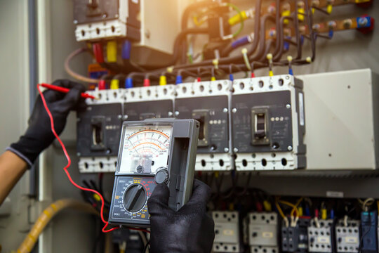 Electrician holding electrical measuring tool meter on panel circuit breaker power electricity switchboard system cabinet for repairing or safety service maintenance and electric cable wiring check.