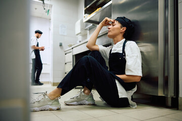 Exhausted female chef sitting on  floor in  kitchen.
