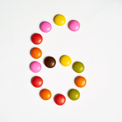 Colored chocolate coated candy alphabet on white background. 6