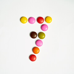 Colored chocolate coated candy alphabet on white background. 7