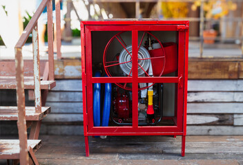 Locked red emergency street cabinet with fire hose reel and blue rolled pipe. Fire safety concept background.