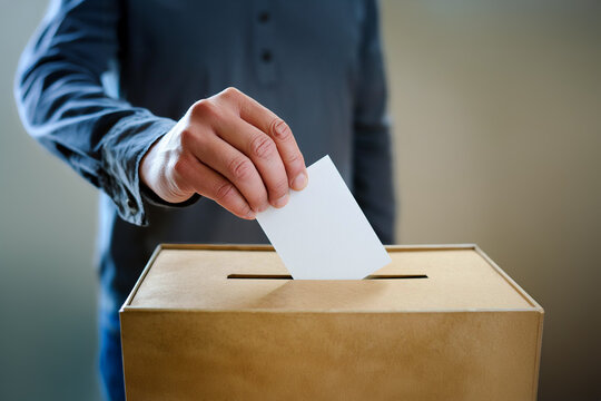 Man's hand placing voting slip into a ballot box. Close up on hand. Person voting during an election or referendum concept.