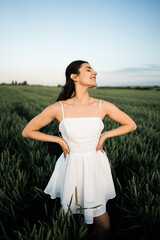 Beautiful woman in a white dress posing and dancing in a green wheat field. Freedom concept.Photo session in a green wheat field