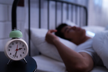 Asian healthy man excellent REM and deep sleep in bed with lucid dream and focus on alarm clock showing 3:33 AM on the bedside table at night