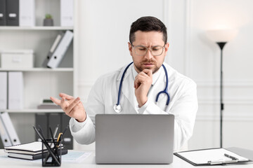 Fototapeta premium Doctor having online consultation via laptop at table in clinic