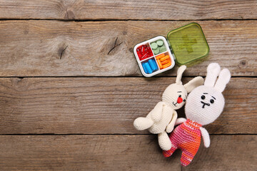 Toy bunnies and pills on wooden background, flat lay. Space for text