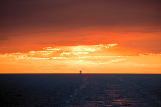 A large ship silhouetted on the horizon of the Mediterranean sea against a dramatic orange sunset