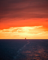 A large ship silhouetted on the horizon of the Mediterranean sea against a dramatic orange sunset