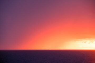 A large motor yacht passing a large storm on the horizon of the Mediterranean sea against a dramatic orange sunset