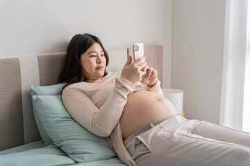 Pregnant asian woman holding smartphone at home using mobile app for pregnant women