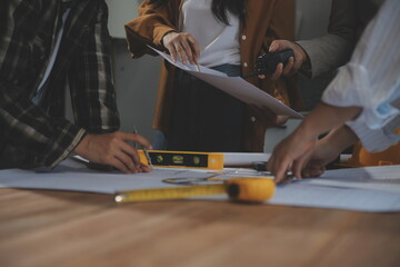 Team of multiethnic architects working on construction plans in meeting room. Engineers discussing on project in office. Mature businessman and woman standing around table working on blueprint.