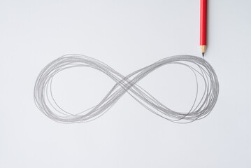 Flat lay red pencil hand drawing infinity symbol on white paper background. Infinity, endless concept.