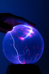a hand touching plasma ball with electric rays on blue background.
