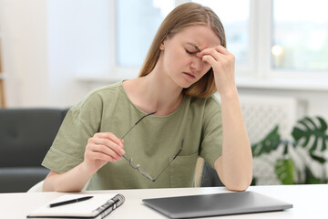 Overwhelmed young woman sitting with laptop at table in room