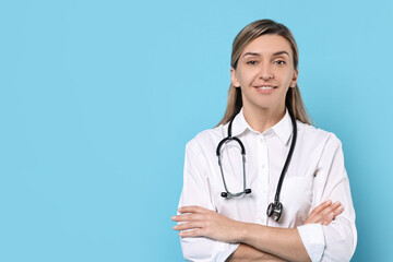 Portrait of happy doctor with stethoscope on light blue background, space for text