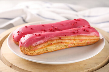 Plate with tasty glazed eclairs on wooden board, closeup