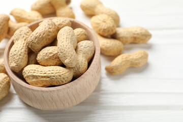 Fresh peanuts in bowl on white wooden table, closeup