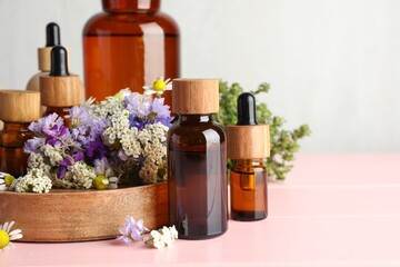 Aromatherapy. Different essential oils and flowers on pink wooden table, space for text