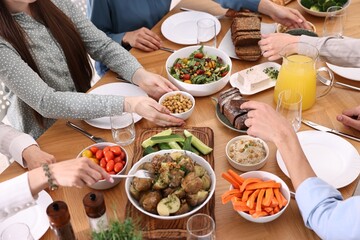 Friends eating vegetarian food at wooden table indoors, closeup