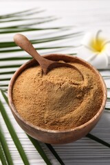 Coconut sugar and spoon in bowl on white wooden table, closeup