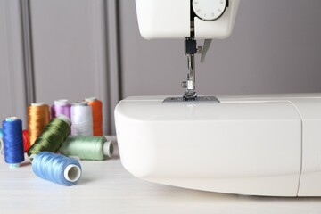 Sewing machine and spools of threads on white wooden table, closeup