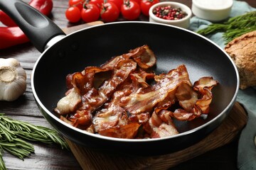 Delicious bacon slices in frying pan and products on wooden table, closeup