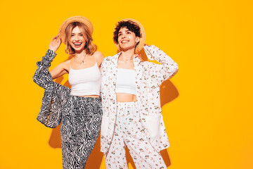 Two young beautiful smiling brunette hipster female in trendy summer costume clothes. Sexy women posing near yellow wall in studio. Positive models having fun. Cheerful and happy