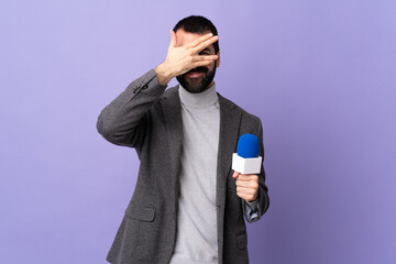 Adult reporter man with beard holding a microphone over isolated purple background covering eyes by...
