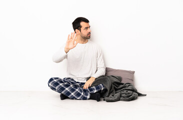 Caucasian man in pajamas sitting on the floor at indoors making stop gesture and disappointed
