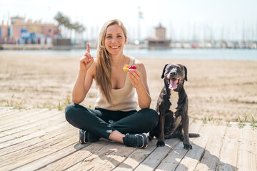 Young blonde woman with her dog holding a tartlet at outdoors pointing up a great idea