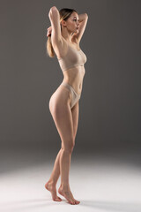 Fototapeta premium Perfect body shape. Portrait of woman with slim fit figure in gray inner wear posing on grey studio background.