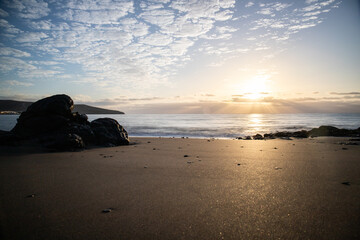 View of the sunrise over the Atlantic Ocean. Fantastic clouds and a bay with a stone beach on a volcanic island. Cold lava stones by the sea at Playa de Tarajalejo beach, Fuerteventura, Canary Islands