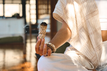 Yogi woman holding scented herbal stick in hand doing yoga breathing exercises. Burning aromatic...