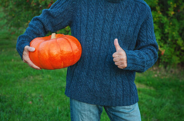 Man holding big orange pumpkin and showing thumbs up. Autumn Halloween concept
