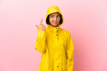 Young latin woman wearing a rainproof coat over isolated background making the gesture of madness putting finger on the head