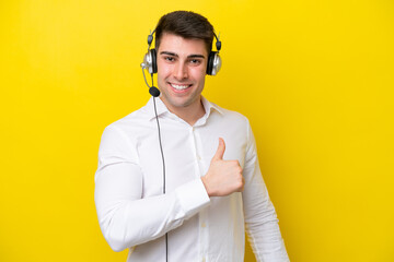 Telemarketer caucasian man working with a headset isolated on yellow background giving a thumbs up gesture