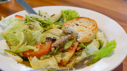Close up of vegetable salad with olives, beef, cheese and slice of bread on a white plate
