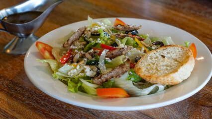 Close up of vegetable salad with beef olives, cheese and slice of bread on a white plate