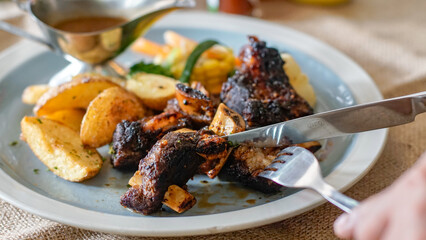 Close up view of  person cuts grilled spare ribs with knife and fork