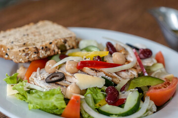 Close up of vegetable salad with olives, cheese and slice of bread on a white plate