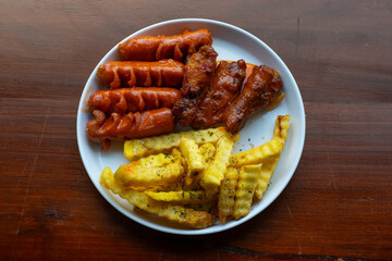 mixed sausage, french fries, and chicken wings cafe platter. Served on white plate, over wooden table surface, in cafe environment