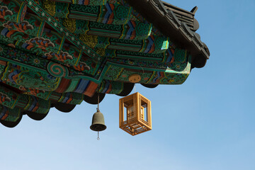 View of the lantern and bell hanging from the wooden eaves of the Buddhist temple building