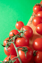 Cherry tomatoes on wooden board on green background. Copy space
