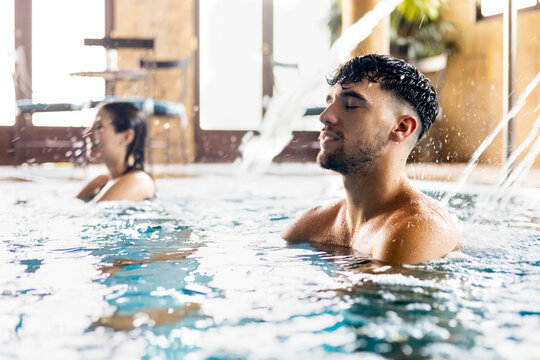 A young couple enjoy themselves in a wellness center. The young people are in a pool at a spa relaxing with pressurized water. Concept of couples between 20 and 30 years old in a spa.
