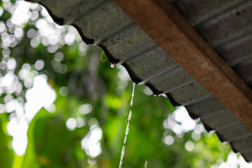Rainwater dripping from a metal roof during a rainy day with green foliage bokeh in the background