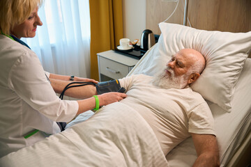 Old bald patient has his blood pressure measured