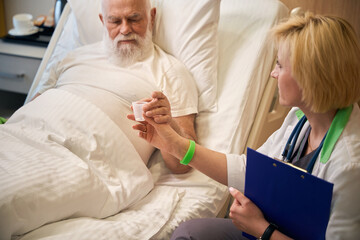 Doctor handing pills to old patient on bed