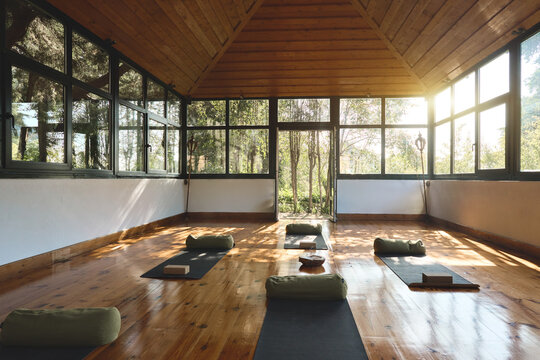 Place for yoga exercises group meditation practices retreats sessions background in natural forest garden area building. Empty clean yoga gym room studio interior with big windows mats on wooden floor