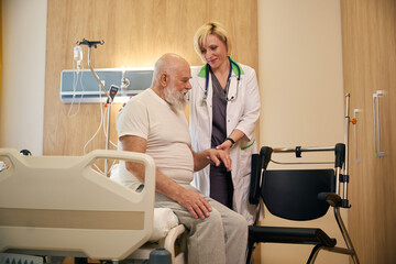 Lady doctor helps an old patient transfer to a wheelchair